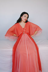 Women's vintage 1980's maxi dress in peach coral color with a V shaped neckline, cape like sleeves, and flower on chest