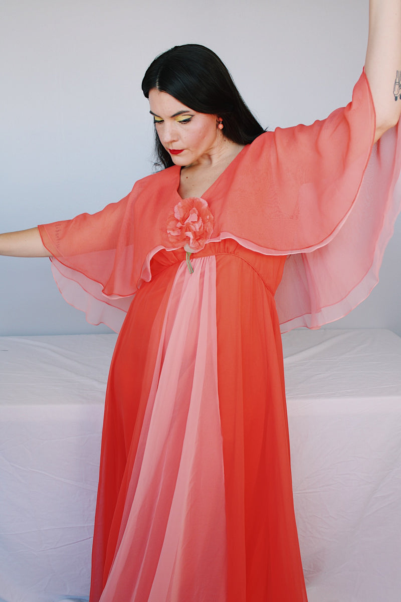 Women's vintage 1980's maxi dress in peach coral color with a V shaped neckline, cape like sleeves, and flower on chest