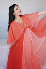 Women's vintage 1980's maxi dress in peach coral color with a V shaped neckline, cape like sleeves, and flower on chest