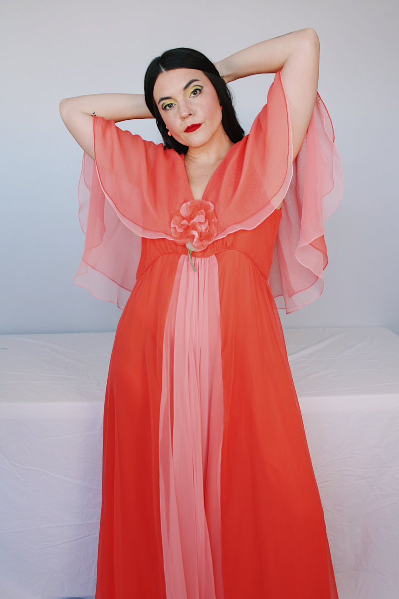 Women's vintage 1980's maxi dress in peach coral color with a V shaped neckline, cape like sleeves, and flower on chest