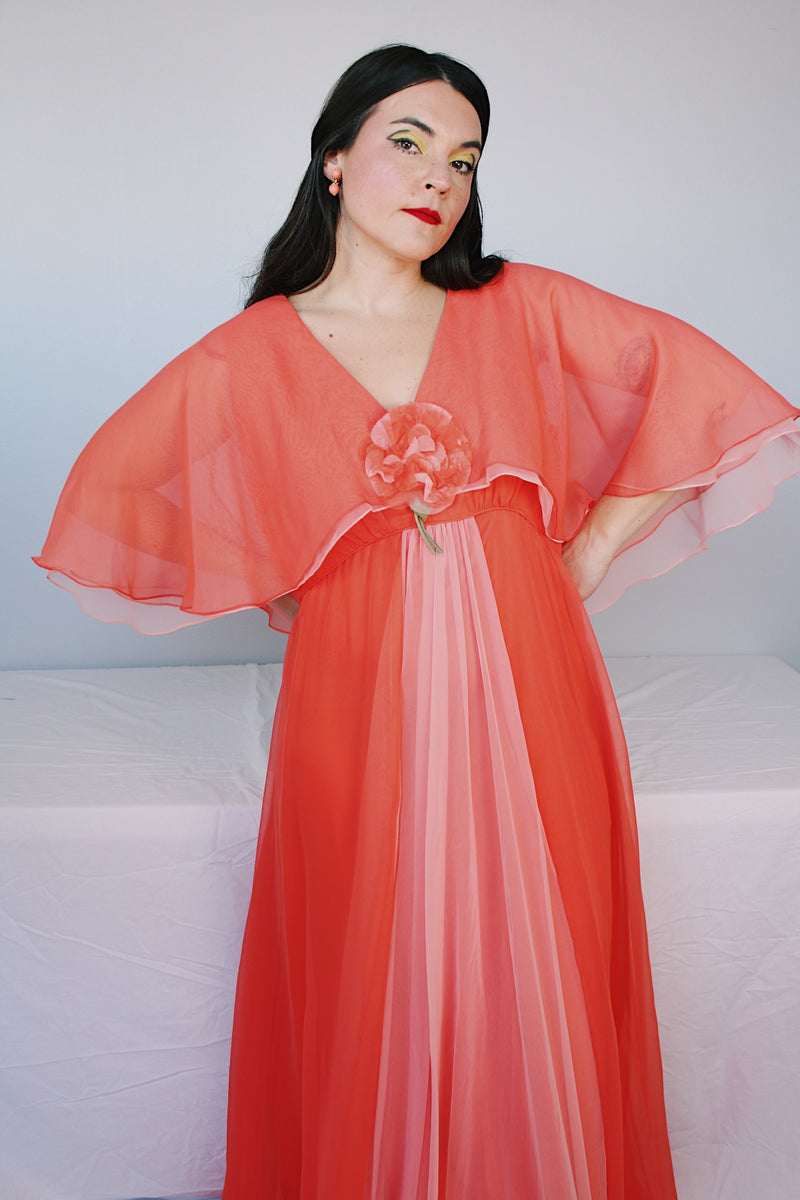 Women's vintage 1980's maxi dress in peach coral color with a V shaped neckline, cape like sleeves, and flower on chest