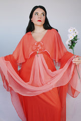 Women's vintage 1980's maxi dress in peach coral color with a V shaped neckline, cape like sleeves, and flower on chest