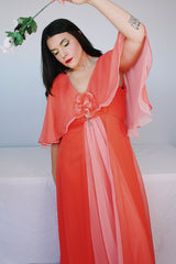 Women's vintage 1980's maxi dress in peach coral color with a V shaped neckline, cape like sleeves, and flower on chest