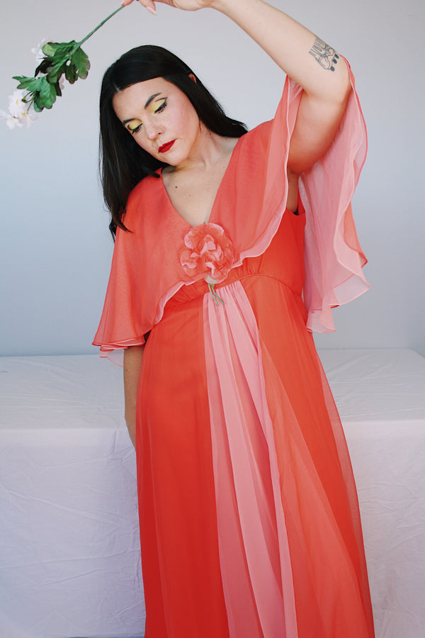 Women's vintage 1980's maxi dress in peach coral color with a V shaped neckline, cape like sleeves, and flower on chest