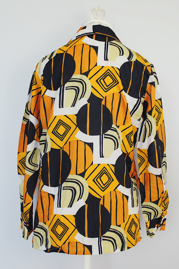 long sleeve button up polyester blouse with double lapel in an abstract orange green and black print 1970's