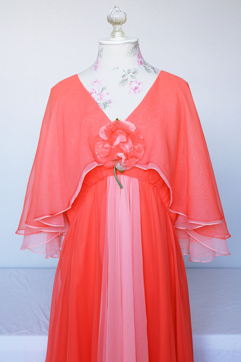 Women's vintage 1980's maxi dress in peach coral color with a V shaped neckline, cape like sleeves, and flower on chest