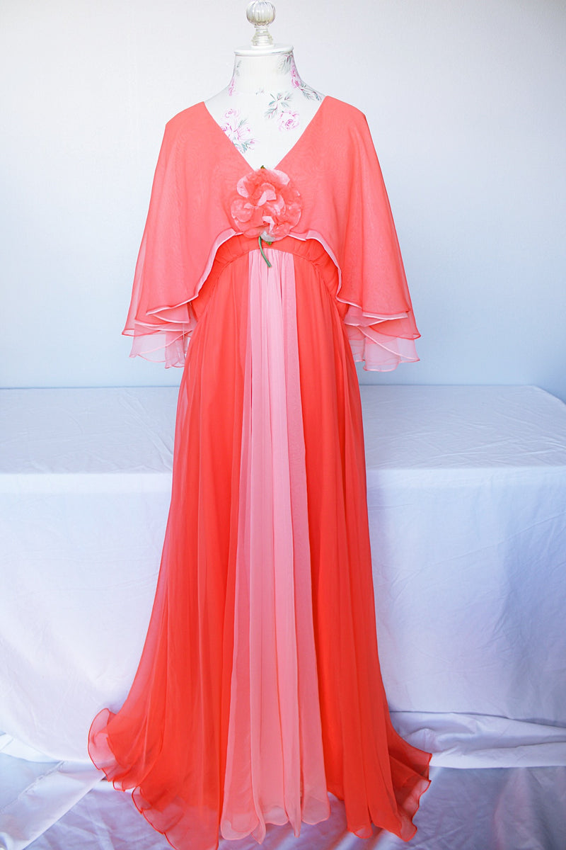 Women's vintage 1980's maxi dress in peach coral color with a V shaped neckline, cape like sleeves, and flower on chest