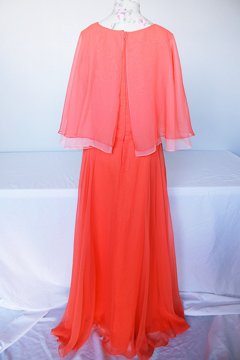 Women's vintage 1980's maxi dress in peach coral color with a V shaped neckline, cape like sleeves, and flower on chest