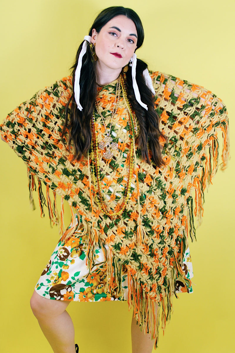 Women's vintage 1970's acrylic knit multicolored poncho with a long fringe trim hem, drawstring at neck, and V shaped neckline in orange, mustard yellow, and olive  green colors.