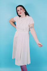 Women's vintage 1970's short sleeve capped sleeved midi length off white cream dress with draped neckline, attached tie bow on shoulder, elastic waistband, and detachable matching tie belt