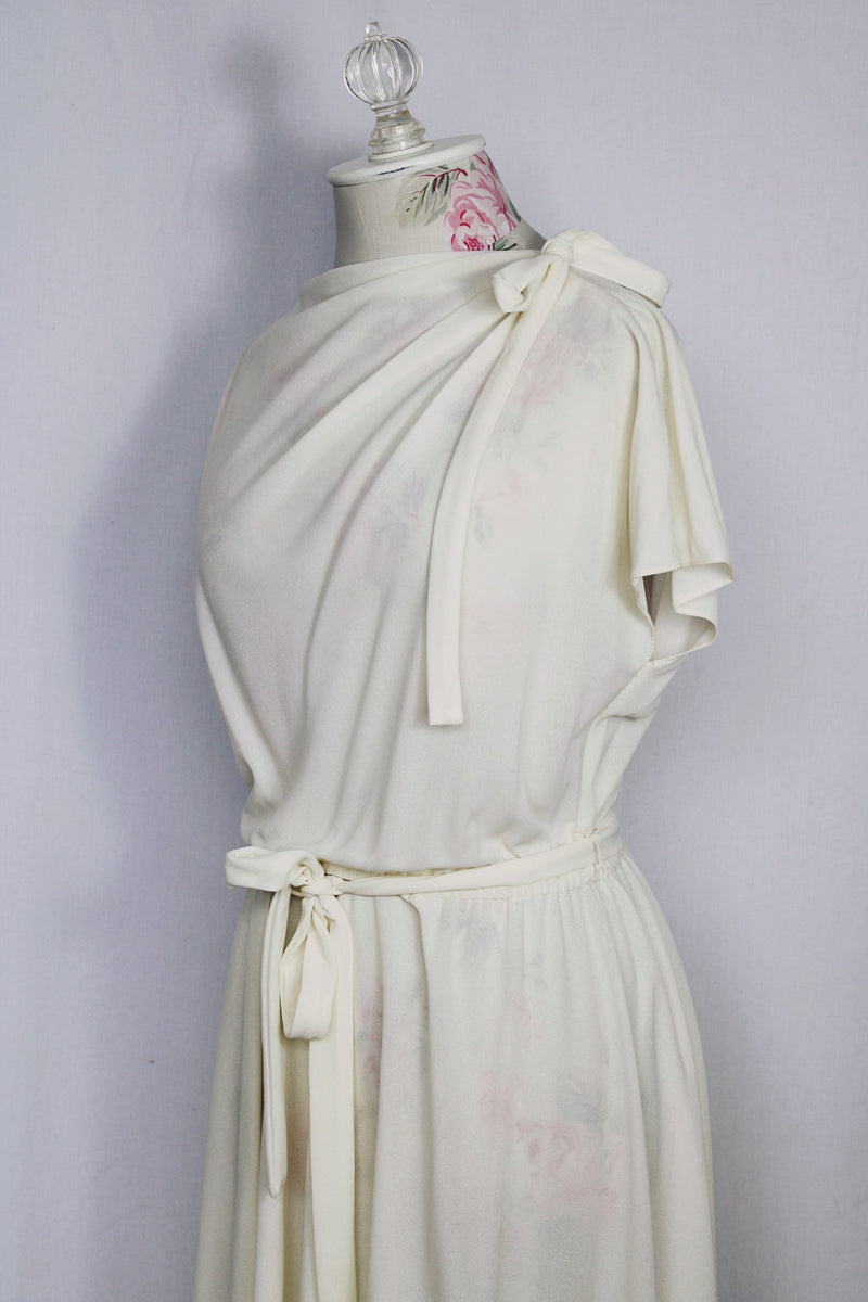 Women's vintage 1970's short sleeve capped sleeved midi length off white cream dress with draped neckline, attached tie bow on shoulder, elastic waistband, and detachable matching tie belt