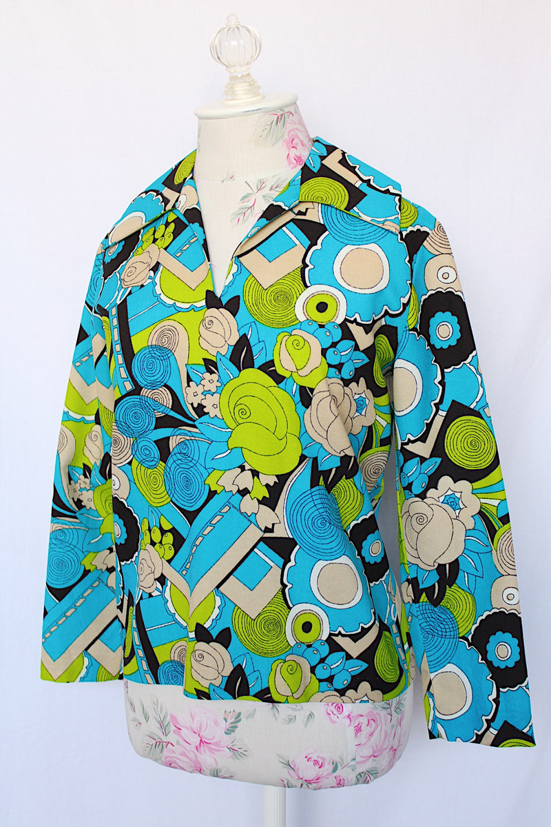 Women's vintage 1970's long sleeve collared blouse with zipper in the back and V shaped neckline. Polyester material in green and blue all over print.