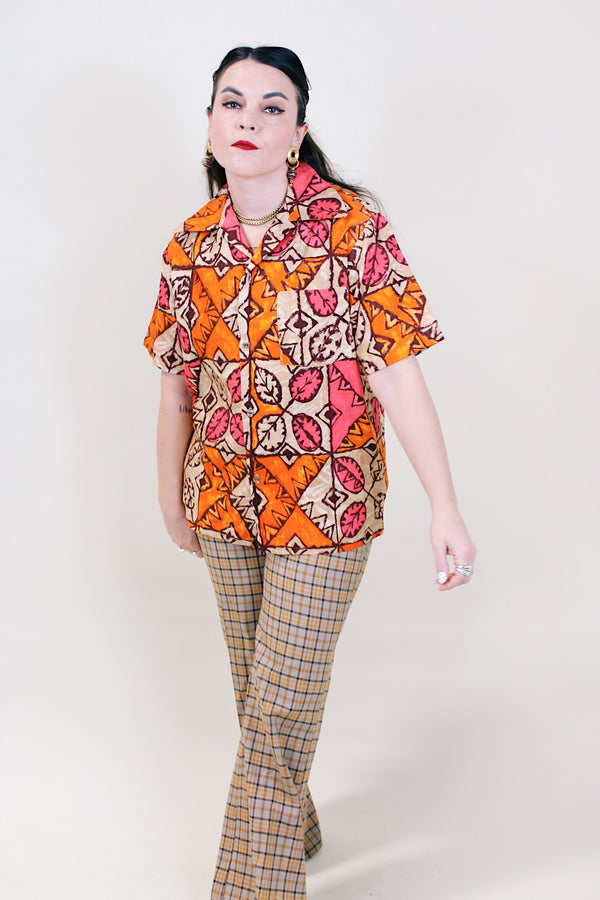 Women's or men's vintage 1960's made in Hawaii short sleeve button up shirt with pointy collar in cotton material with all over tan, orange, and pink Hawaiian print. 