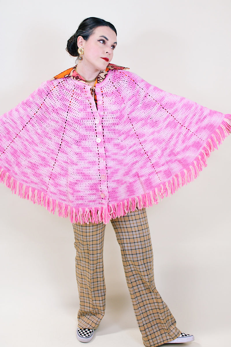 Women's vintage 1970's pink colored crochet knit poncho in soft acrylic material. Fringe trim hem and buttons up the front.