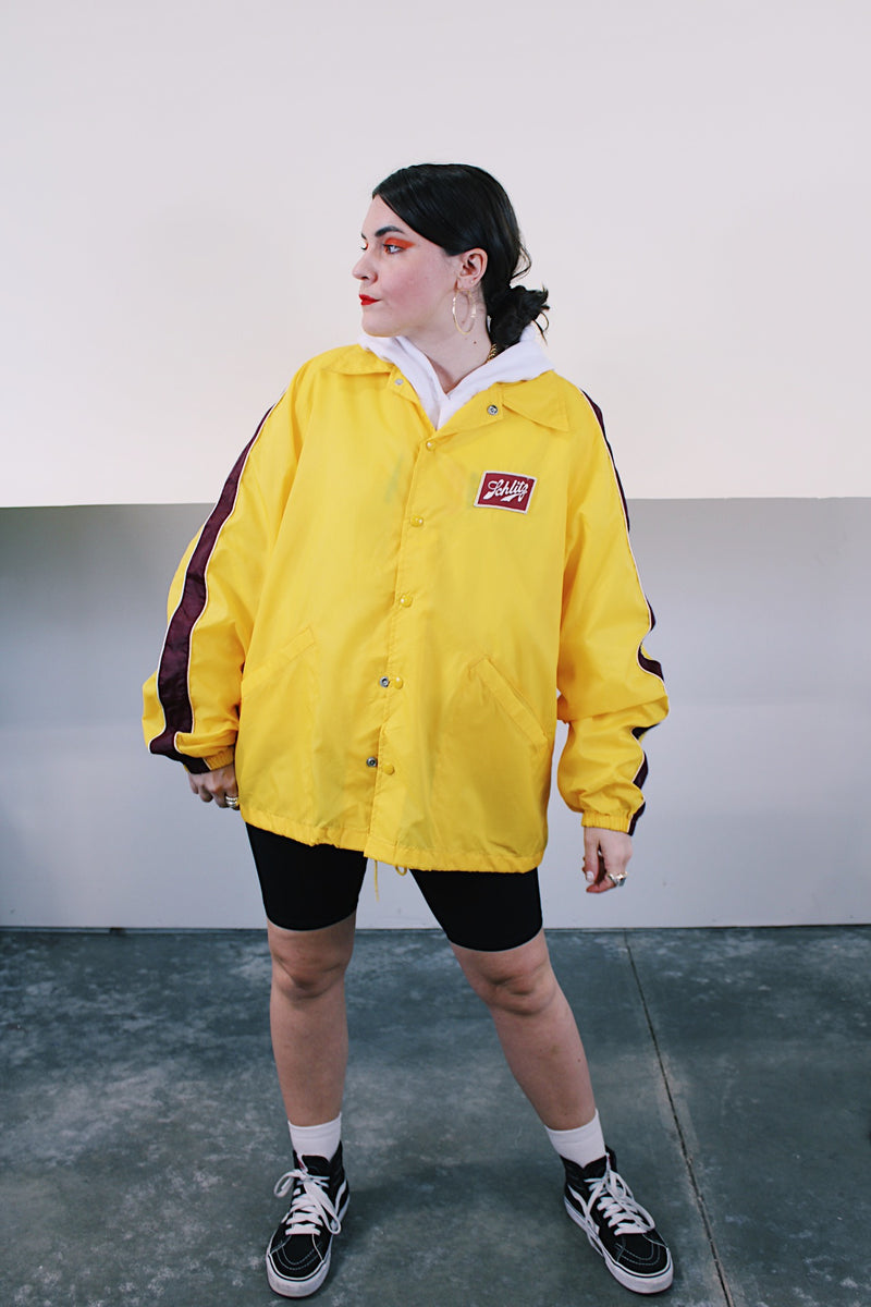 Women's or mens' vintage 1970's Swingster, World of Wearables label long sleeve yellow lightweight windbreaker with popper buttons and a maroon stripe on each arm. Schlitz patch on left chest