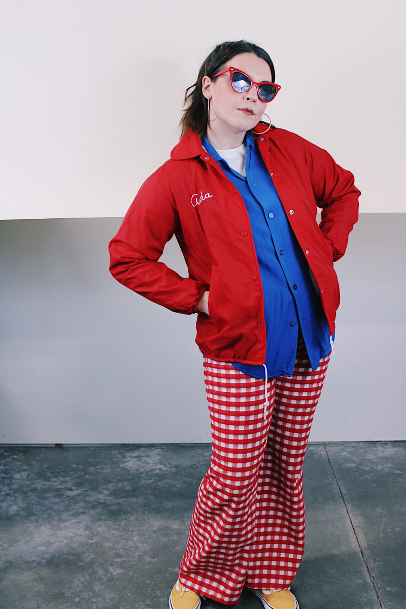 Women's vintage 1970's Pla-Jac by Dunbrooke, Made in USA label long sleeve red nylon windbreaker with popper buttons, cotton liner, round collar, and white graphic.