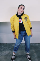Women's or men's vintage 1970's long sleeve yellow nylon zip up bomber jacket with black knit trim and black graphic on left chest. 