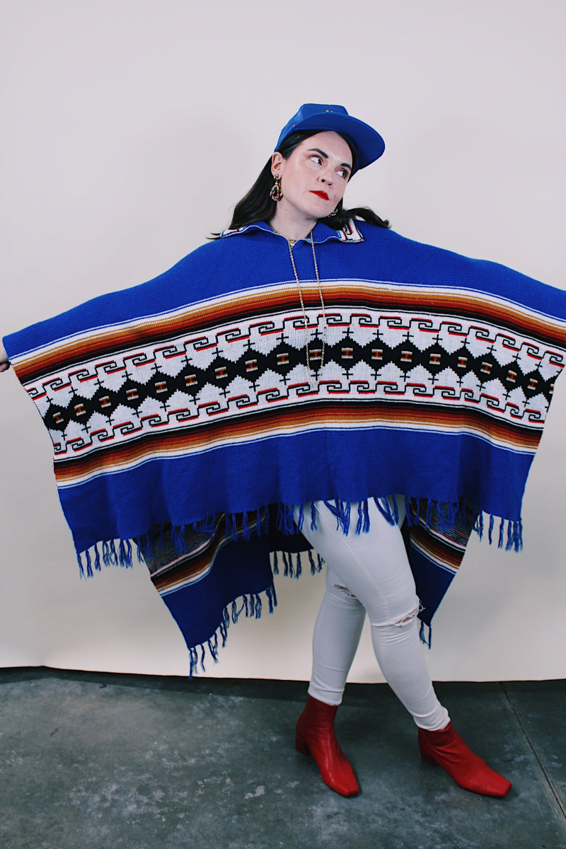 Women's or men's vintage 1970's blue acrylic material poncho with fringe trim and half zipper closure at neck. White. black, brown, and red striped print. 