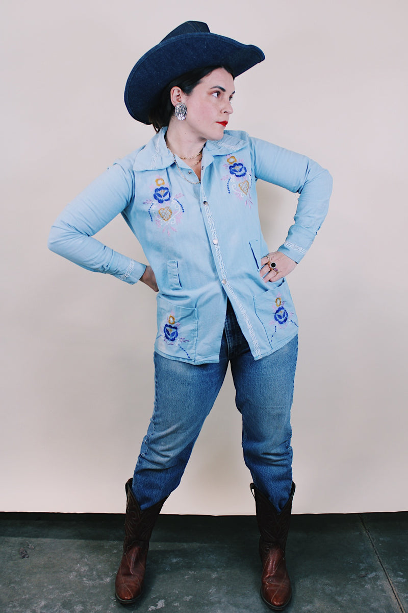 Women's or men's vintage 1970's long sleeve light wash denim shirt with popper buttons, pockets, belt loops, and floral embroidery throughout. 