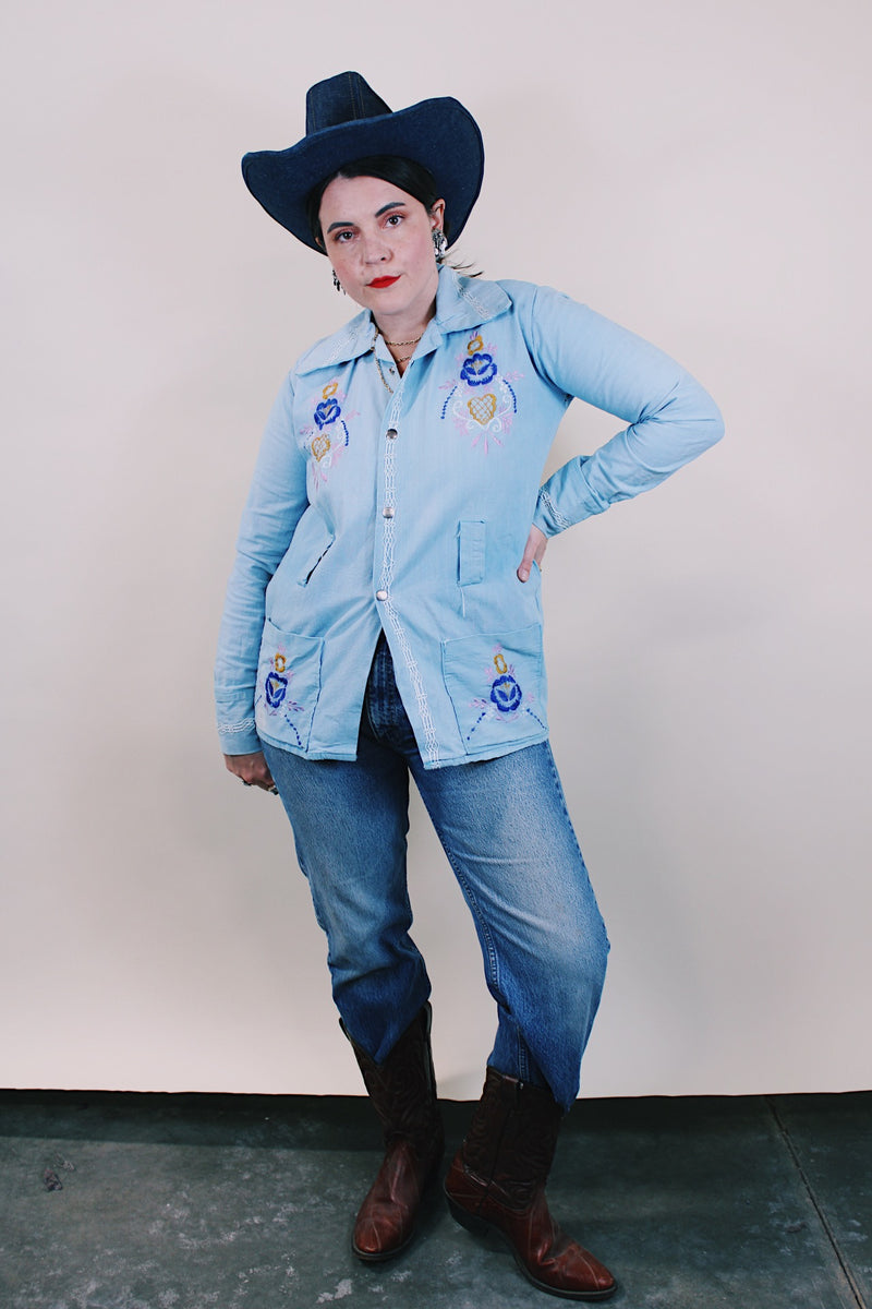 Women's or men's vintage 1970's long sleeve light wash denim shirt with popper buttons, pockets, belt loops, and floral embroidery throughout. 