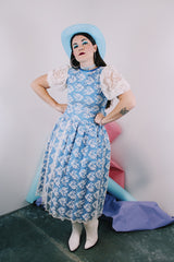 Women's vintage 1980's blue polyester dress with a white lace overlay. Has sheer puff sleeves, side zipper, low cut back, and a lace bow in the back