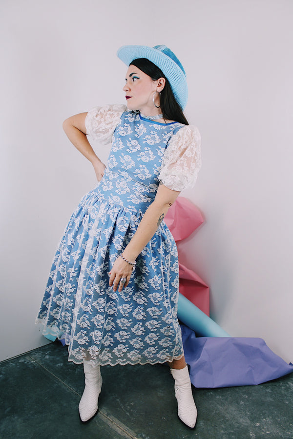 Women's vintage 1980's blue polyester dress with a white lace overlay. Has sheer puff sleeves, side zipper, low cut back, and a lace bow in the back