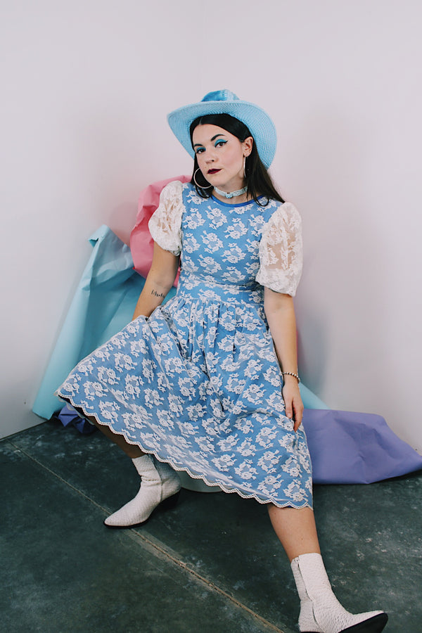 Women's vintage 1980's blue polyester dress with a white lace overlay. Has sheer puff sleeves, side zipper, low cut back, and a lace bow in the back