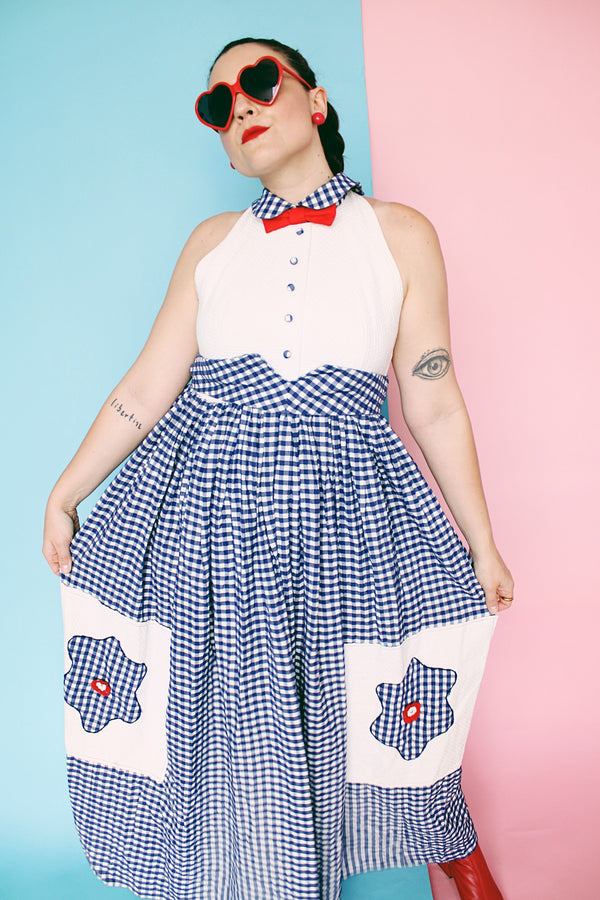 Women's vintage 1970's sleeveless halter neck maxi style halter dress in white and navy gingham print with red bowtie at neck and two front pockets on skirt with flowers. 
