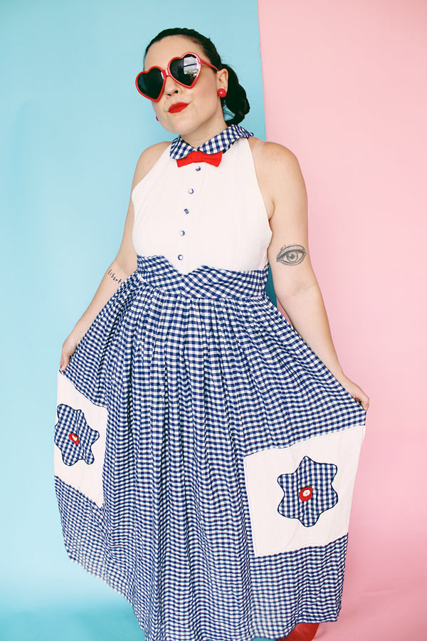 Women's vintage 1970's sleeveless halter neck maxi style halter dress in white and navy gingham print with red bowtie at neck and two front pockets on skirt with flowers. 