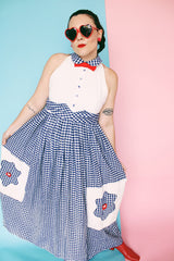 Women's vintage 1970's sleeveless halter neck maxi style halter dress in white and navy gingham print with red bowtie at neck and two front pockets on skirt with flowers. 