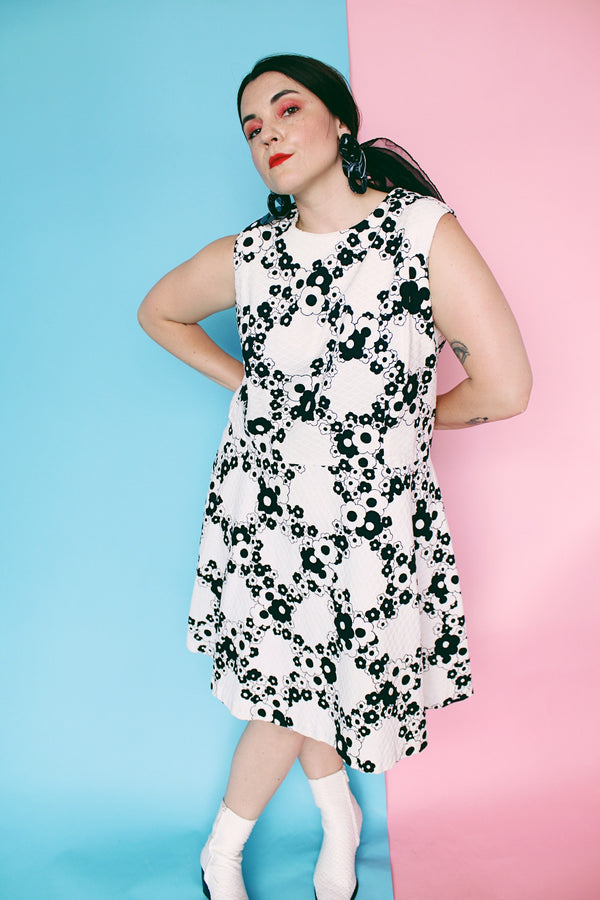 Women's vintage 1970's sleeveless drop waist midi length cotton material dress in white with all over black floral print.