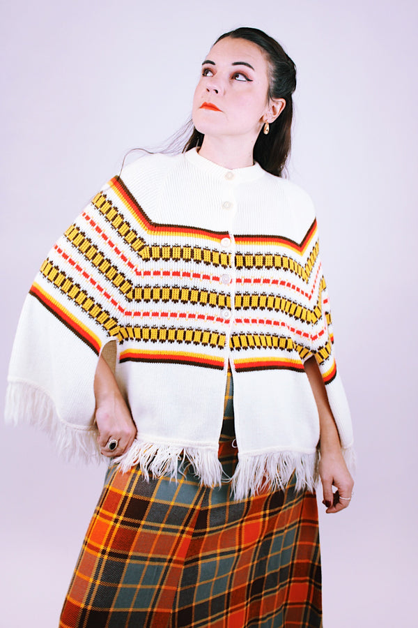 white vintage women's 1960's acrylic knit poncho with striped pattern and fringed hem