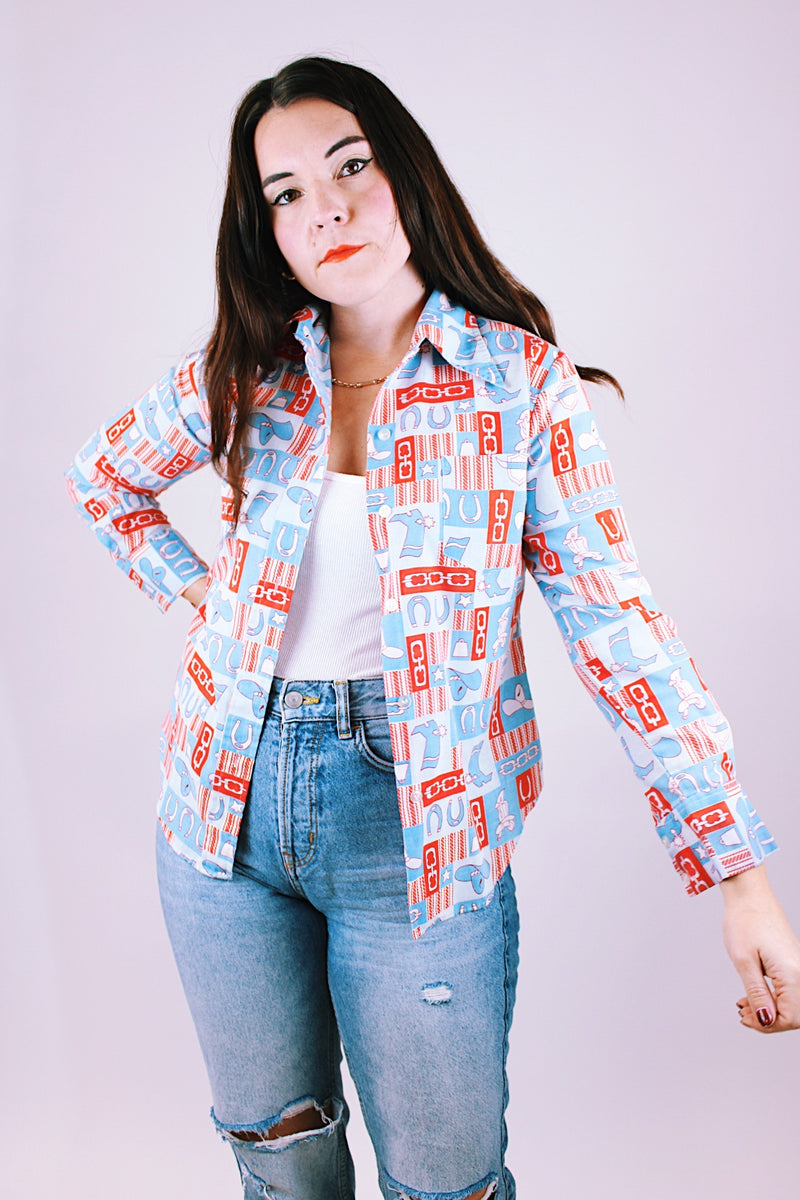 long sleeve 1970's women's vintage button up blouse with collar in a red and blue western print with cowboy hats and boots