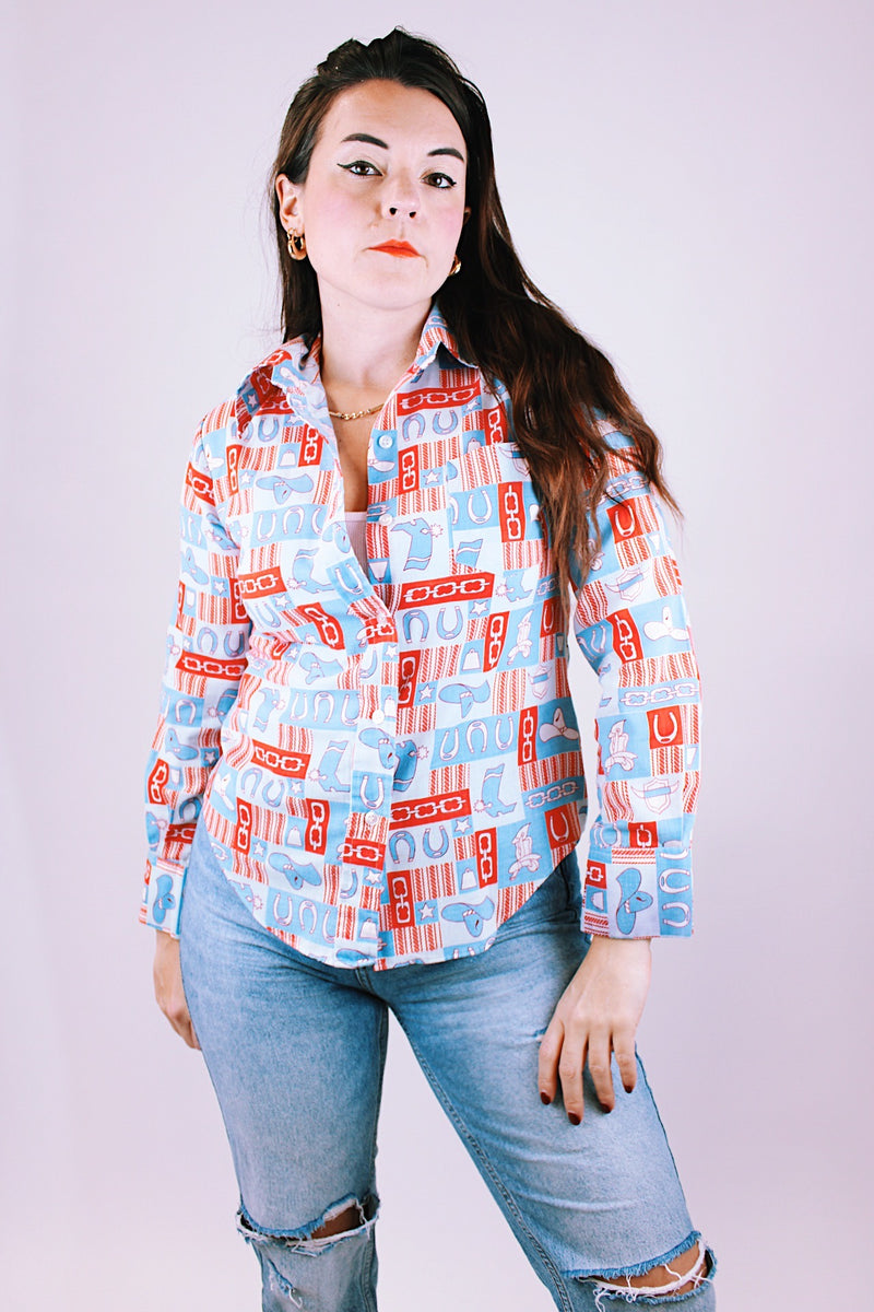long sleeve 1970's women's vintage button up blouse with collar in a red and blue western print with cowboy hats and boots